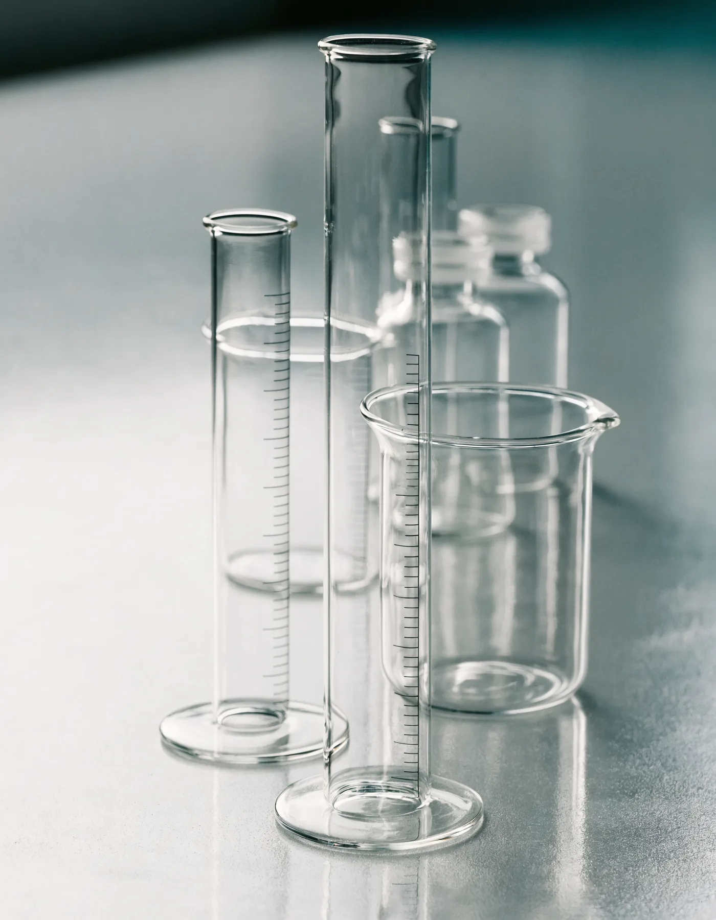 Precision borosilicate laboratory glassware — graduated cylinders, a beaker, and sealed clear-glass storage vials on a lab surface